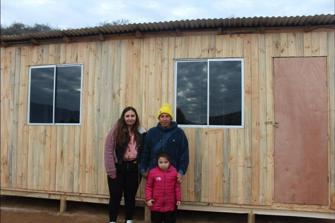 Familia frente a su mediagua de tablas verticales terminada durante las capacitaciones de 2022